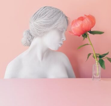 pink flower in vase near female bust