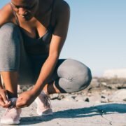 close up photo of woman in gray tank top and gray leggings tying her shoes