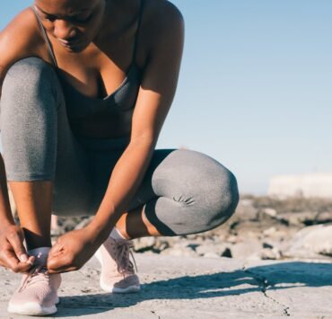 close up photo of woman in gray tank top and gray leggings tying her shoes
