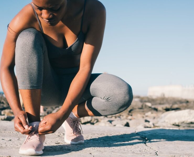 close up photo of woman in gray tank top and gray leggings tying her shoes