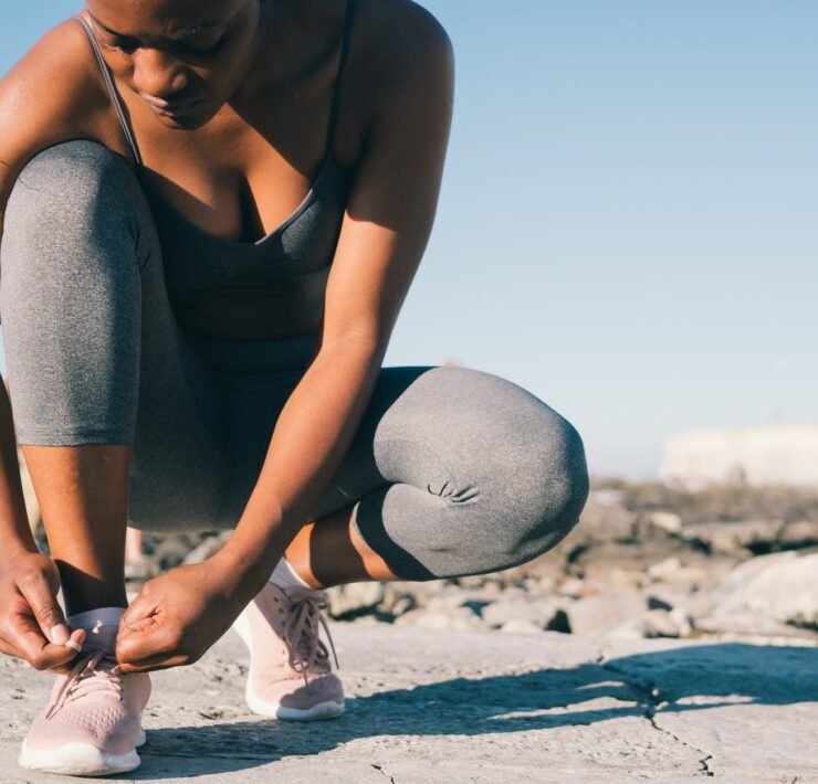 close up photo of woman in gray tank top and gray leggings tying her shoes