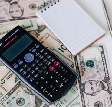 calculator and notepad placed on usa dollars stack