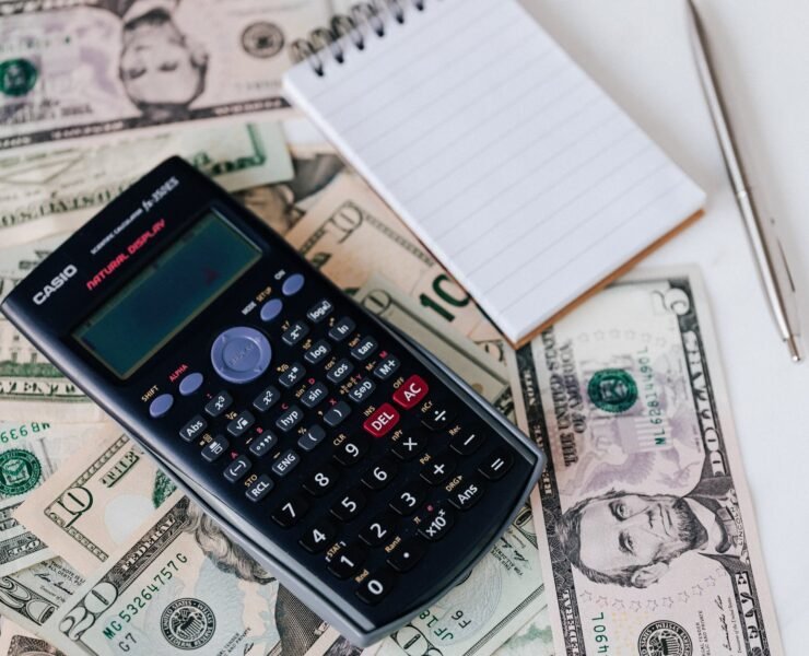calculator and notepad placed on usa dollars stack
